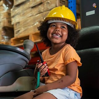 girl sitting on a forklift wearing a hardhat and holding a walkie talkie