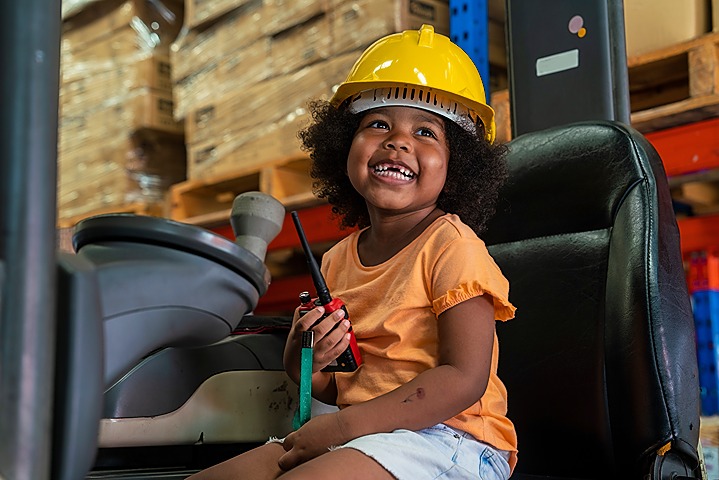 girl sitting on a forklift wearing a hardhat and holding a walkie talkie